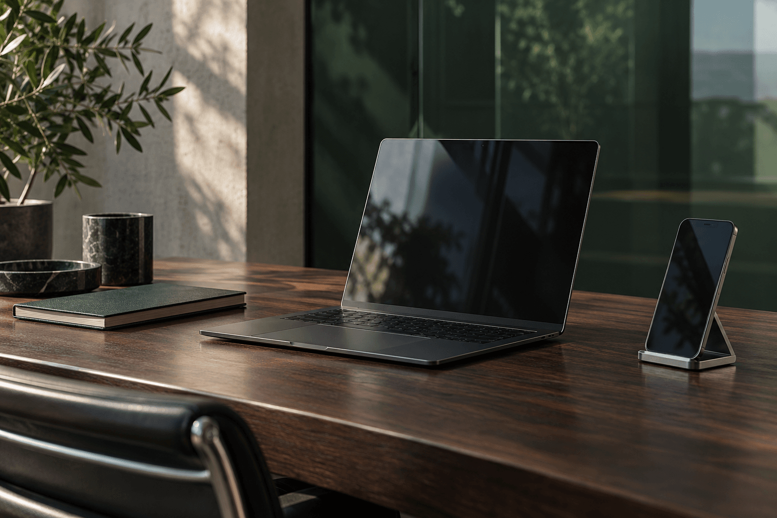 A considered workspace with a graphite laptop, phone and notebook in natural light